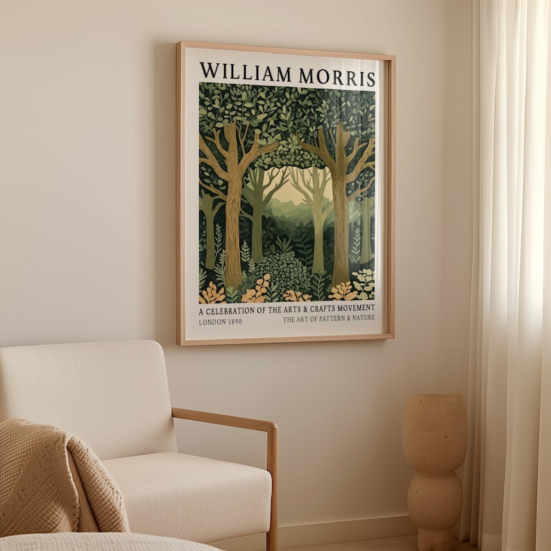 William Morris forest scene art print in a natural wood frame displayed above a light beige armchair. The artwork depicts a trio of elegant trees, their branches stretching upward and crowned with a canopy of patterned leaves in deep and muted greens. Soft golden accents highlight the forest floor, while a distant pale yellow sky glows between the trees. The design is framed with bold typography at the top and historical reference text at the bottom.