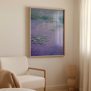 Op de afbeelding: Een ingelijste kunstdruk die een serene waterpartij weergeeft met waterlelies en roze bloemen die op het wateroppervlak drijven. Het kunstwerk is ingelijst in een lichtgekleurde houten lijst en hangt aan een neutraal gekleurde muur.