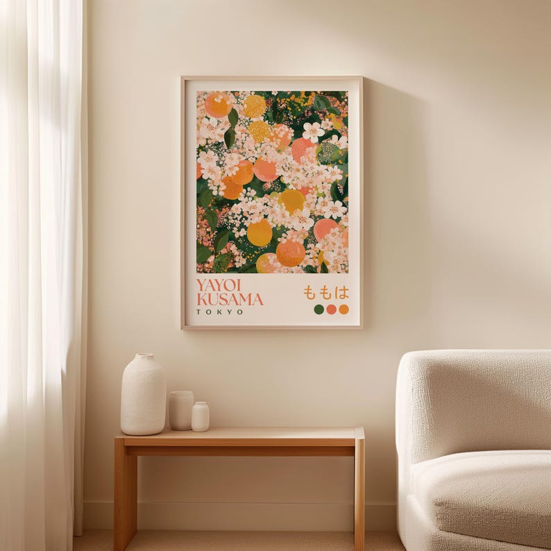 Framed Yayoi Kusama-inspired floral print laid flat on a neutral surface, surrounded by wrapping paper. The detailed design features peach blossoms and fruit with intricate dot patterns and rich greens, pinks, and oranges.