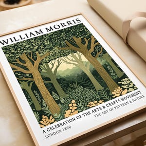Close-up of a William Morris forest scene art print in a natural wood frame, lying flat on a table beside brown paper wrapping. The illustration highlights the intricate leaf patterns, textured tree trunks, and golden flower details at the forest edge, with misty green hills and a pale yellow sky in the background. Bold black text frames the design, honouring the Arts & Crafts Movement and its dedication to the beauty of nature.