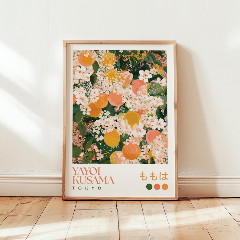 Poster of a Yayoi Kusama-inspired floral design featuring blooming peach blossoms and round peach fruits in soft pink, orange, and yellow tones, set against a deep green background. Displayed in a natural wood frame, leaning against a white wall on a light wooden floor with sunlight streaming in.