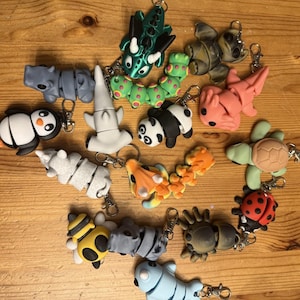 May include: A collection of 15 colorful animal keychains, including a panda, a turtle, a ladybug, a bee, a seahorse, a shark, a penguin, a dragon, a fish, and a crab. The keychains are made of plastic and have a variety of colors and designs.