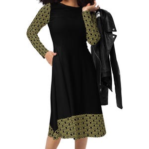 May include: Black dress with long sleeves featuring a gold wave pattern on the sleeves and hem. The dress has a round neckline and a fitted bodice that flows into a flared skirt. A black leather jacket is held over the shoulder.
