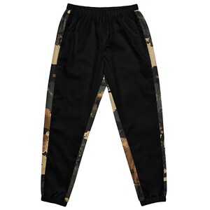 May include: Black track pants with a camouflage pattern down the sides. The camouflage design features shades of brown, tan, and green. The pants have an elastic waistband and cuffs.