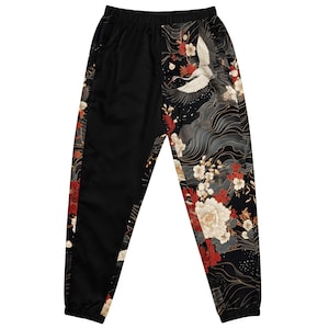 May include: Black track pants with a floral and crane design. The pants feature a black background with a detailed pattern of white, red, and gold flowers, and a crane in flight. The design is on the right leg and a stripe on the left leg.