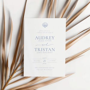 May include: A white wedding invitation with blue text and a seashell graphic. The invitation includes the names Audrey and Tristan, the date September 21, 2028, and the location, The Lighthouse Estate, Cape Cod, Massachusetts. Dried palm leaves are in the background.