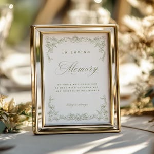 May include: A gold-colored rectangular picture frame with the words "IN LOVING Memory" and the text "OF THOSE WHO COULD NOT BE HERE WITH US TODAY BUT ARE FOREVER IN OUR HEARTS" printed on a white background. The frame has decorative floral accents.