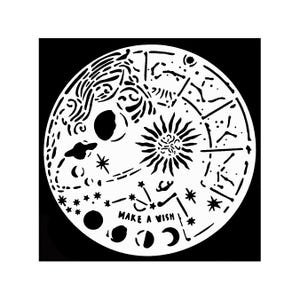 May include: A circular white stencil featuring celestial motifs including a sun, moon phases, stars, planets, and constellations. The design includes the text "MAKE A WISH" in capital letters, set against a solid black background.