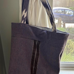 May include: A purple tote bag with a white and black geometric pattern on the handles and a brown and white stripe down the front.