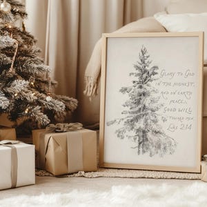 May include: A framed print featuring a pencil sketch of a Christmas tree and the text "Glory to God in the highest, and on earth peace, good will toward men Luke 2:14." The print is next to a decorated Christmas tree and wrapped gifts.
