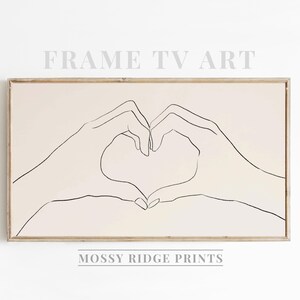 May include: Framed wall art featuring a minimalist line drawing of two hands forming a heart shape. The artwork is in a light beige color, with black outlines. The text "FRAME TV ART" and "MOSSY RIDGE PRINTS" are displayed on the image.