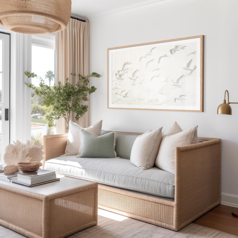 May include: A light gray linen sofa with a woven rattan frame and a light green throw pillow. The sofa is in a living room with a large framed print of birds in flight on the wall behind it.