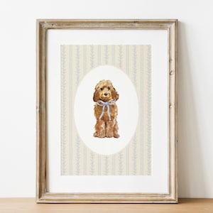 May include: Framed watercolor print of a brown dog with a blue bow, set against a cream and blue floral wallpaper background. The dog is centered in an oval frame. The artwork is displayed in a wooden frame.