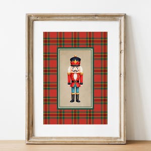 Pode incluir: Impressão emoldurada com uma ilustração colorida de um soldado quebra-nozes. A obra de arte está sobre um fundo xadrez vermelho e verde, emoldurada por uma moldura de madeira dourada. O quebra-nozes veste um casaco vermelho, calças azuis e um chapéu preto.