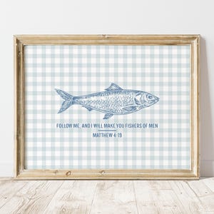 Könnte beinhalten: Gerahmter Druck mit einer blauen Fischillustration auf einem hellblau-weiß karierten Muster. Der Text "Follow me, and I will make you fishers of men Matthew 4:19" steht unter dem Fisch. Der Rahmen ist hellbraun.