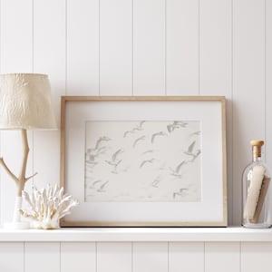 May include: A white wooden shelf with a white lamp with a cream-colored shade, a framed print of a flock of birds in flight, and a clear glass bottle with a cork stopper.