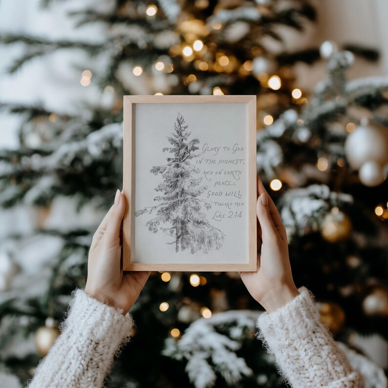 May include: A framed pencil drawing of a Christmas tree with the text "Glory to God in the highest, and on earth peace, good will toward men. Luke 2:14." The frame is light brown, and the background is a blurred Christmas tree with lights.