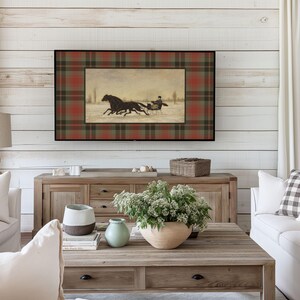 K&ouml;nnte beinhalten: Ein gerahmtes Kunstwerk mit einer Winterszene mit Pferden, die einen Schlitten ziehen, vor einem karierten Hintergrund in Rot, Gr&uuml;n und Braun. Das Kunstwerk wird &uuml;ber einem Holzschrank in einem Wohnzimmer pr&auml;sentiert.