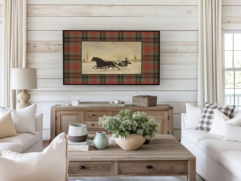 K&ouml;nnte beinhalten: Ein gerahmtes Kunstwerk mit einer Winterszene mit Pferden, die einen Schlitten ziehen, vor einem karierten Hintergrund in Rot, Gr&uuml;n und Braun. Das Kunstwerk wird &uuml;ber einem Holzschrank in einem Wohnzimmer pr&auml;sentiert.
