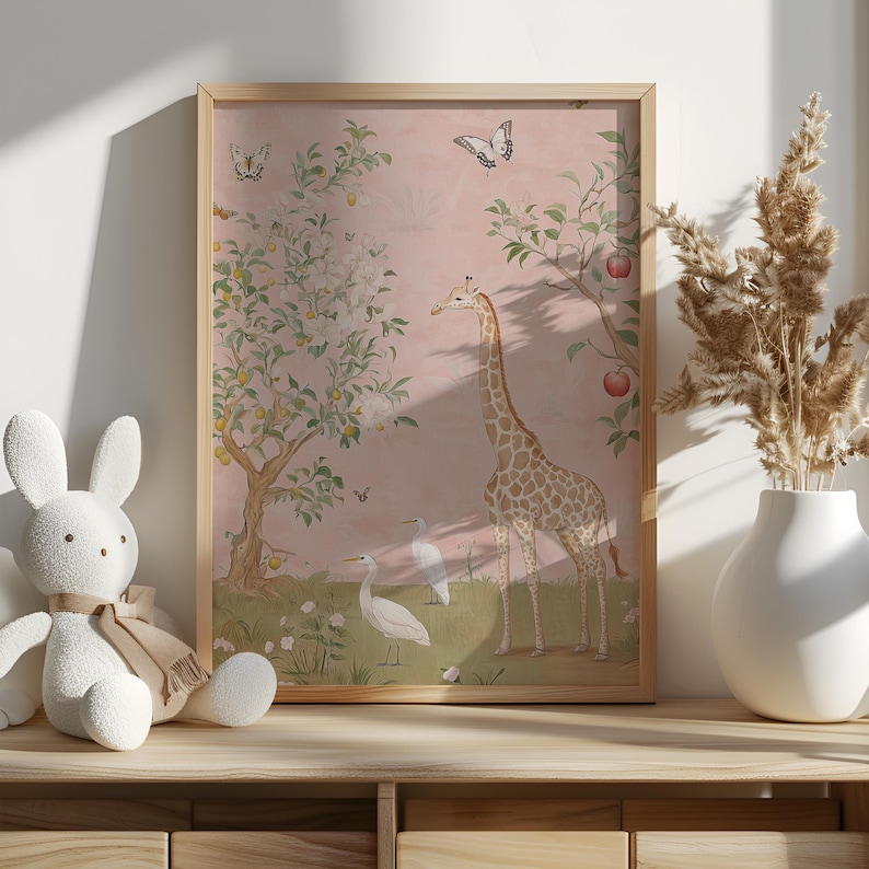 May include: A framed art print featuring a giraffe, birds, and butterflies in a whimsical garden scene. The artwork has a soft pink background with trees bearing fruit. The frame is a light wood color.