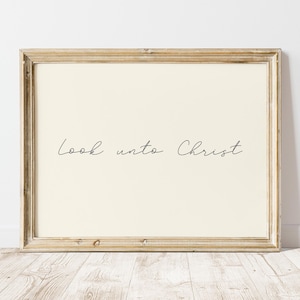 May include: A framed print with the words "Look unto Christ" in elegant cursive script. The text is in black against a cream-colored background. The frame is a light, distressed wood.