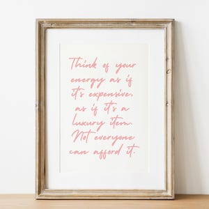 Può includere: Stampa incorniciata con il testo "Think of your energy as if it's expensive, as if it's a luxury item. Not everyone can afford it." Il testo rosa è su sfondo bianco, in una cornice di legno.