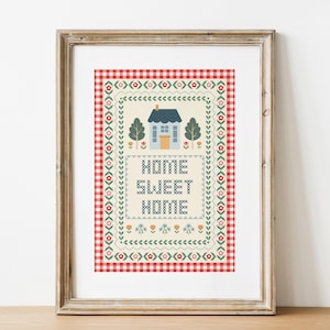 Puede incluir: Arte de punto de cruz enmarcado con un tema campestre. La obra presenta una casa azul, árboles y las palabras "HOME SWEET HOME" en un marco decorativo. El fondo tiene un patrón de cuadros rojos y blancos.