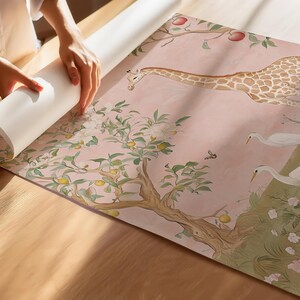 May include: A roll of wallpaper with a whimsical design featuring a giraffe, birds, and a tree with fruit. The wallpaper has a soft pink background with green and brown accents. The image shows the wallpaper being unrolled.