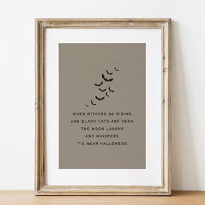May include: A framed Halloween print with a taupe background and black bat silhouettes. The text reads: "When witches go riding, and black cats are seen. The moon laughs and whispers. 'Tis near Halloween."