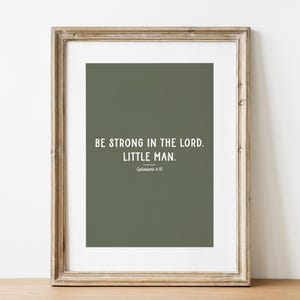 May include: Framed print with the text "BE STRONG IN THE LORD. LITTLE MAN." in white on a muted green background. The frame is a light brown color. The text is from Ephesians 6:10.