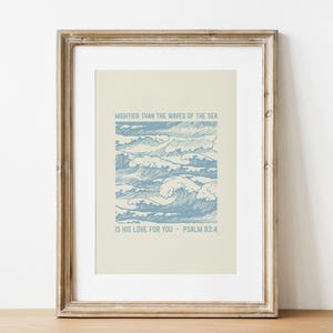 Könnte beinhalten: Gerahmter Kunstdruck mit einer blau-weißen Wellenillustration. Der Druck enthält den Text "MIGHTIER THAN THE WAVES OF THE SEA" und "IS HIS LOVE FOR YOU - PSALM 93:4". Das Kunstwerk ist in einem Holzrahmen.