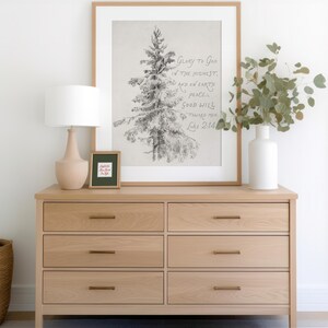 May include: A light oak dresser with six drawers and brass handles, featuring a framed print of a detailed tree sketch. The print includes the text "Glory to God in the Highest, and on Earth Peace, Good Will toward Men, Luke 2:14." A lamp and vase are also on the dresser.