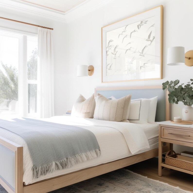 May include: A light blue bed with a white duvet and a light blue throw blanket. The bed has a wooden frame and a light blue headboard. There are two white pillows and two beige pillows on the bed. A nightstand with a lamp and a vase of greenery is next to the bed. A framed print of birds in flight hangs on the wall above the bed.
