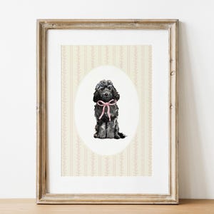 Può includere: Stampa incorniciata con un'illustrazione ad acquerello di un cane nero con un fiocco rosa. Il cane è centrato su un ovale su uno sfondo color crema con un motivo floreale. La cornice è in legno chiaro invecchiato.