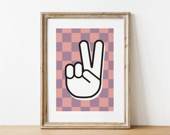 Op de afbeelding: Een ingelijst print met een roze en paarse geruite achtergrond en een wit vredesteken in het midden.