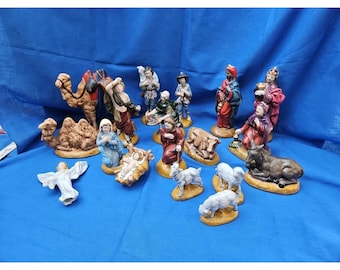 May include: A collection of ceramic nativity figurines, including figures of the Holy Family, angels, shepherds, and the Three Wise Men. The figurines are painted in various colors and set on a blue background.