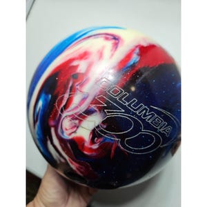 May include: A spherical bowling ball featuring a swirling marbled pattern of deep blue, bright red, and creamy white colors. The surface has a glossy finish with the text Columbia 300 engraved in a bold, stylized font across the center of the ball.