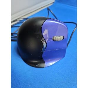 Puede incluir: Un ratón de ordenador con cable, cuerpo negro redondeado y panel lateral derecho de color morado metálico. Incluye una rueda de desplazamiento gris y un pequeño botón plateado con la etiqueta POINTER SPEED entre las secciones negra y morada.