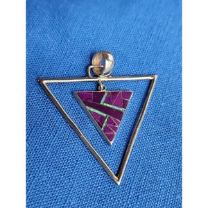May include: A silver-toned pendant with a geometric design. The pendant features a triangle within a triangle, with a mosaic-style inlay of purple and green stones. The pendant hangs from a silver bail.