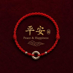 May include: A red braided bracelet featuring a silver ring and two silver beads. The bracelet is set against a dark red background with gold Chinese characters and the words "Peace & Happiness".