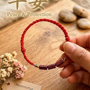 May include: A red braided bracelet with dark brown rectangular beads. The bracelet is held by a hand. The image includes the text "Peace & Protection" and "Handcrafted". The background is a wooden surface.