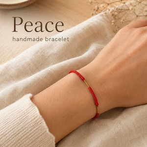 May include: A red handmade bracelet with gold detailing is shown. The word "Peace" is written above the words "handmade bracelet". The bracelet is on a person's wrist. The background is neutral.