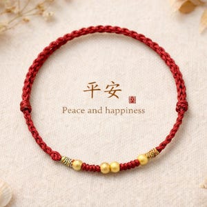 May include: A red braided bracelet with gold beads and accents. The circular bracelet features the text "Peace and happiness" in English and Chinese characters. The bracelet is displayed on a neutral background with decorative elements.