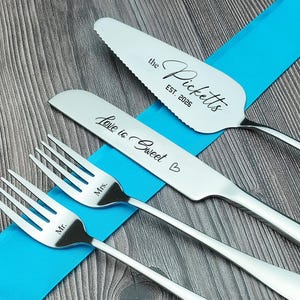 Puede incluir: Un juego de servir pastel de bodas de acero inoxidable con una espátula para pastel, un cuchillo para pastel y dos tenedores. La espátula para pastel está grabada con "the Picketts EST. 2026". El cuchillo está grabado con "Love is Sweet". Los tenedores están grabados con "Mr." y "Mrs."
