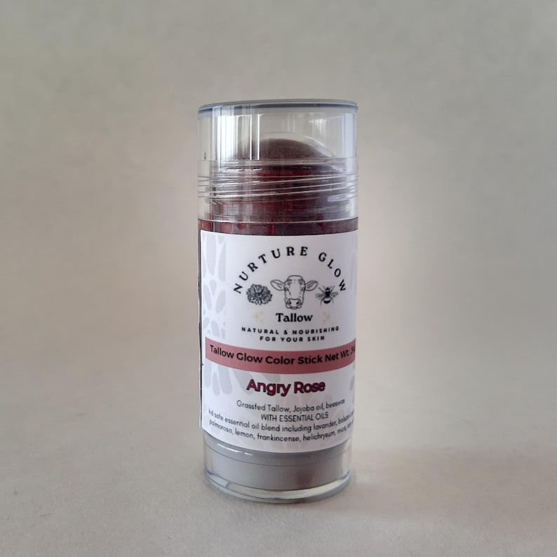 以下が含まれることがあります： Angry RoseのTallow Glow Color Stickが入った透明な円筒形の容器。ラベルには牛のイラストと「Nurture Glow」の文字が描かれています。この製品にはエッセンシャルオイルが含まれており、肌に自然で栄養を与える製品です。