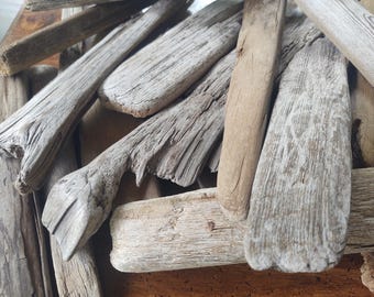 May include: Close-up of weathered driftwood pieces in various shapes and sizes. The wood displays a range of natural colors, from light beige to darker brown, with visible grain and texture. The arrangement suggests a rustic, natural theme.