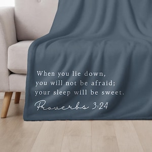 May include: A navy blue throw blanket on a light grey sofa. The blanket has white text: "When you lie down, you will not be afraid; your sleep will be sweet. Proverbs 3:24."