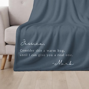 May include: A dark blue fleece throw blanket with white text that reads "Jessica, Consider this a warm hug, until I can give you a real one. -Mark"