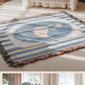 May include: A woven throw blanket featuring a blue and white striped pattern with a central oval graphic of a goose wearing a blue bow. The name SAMMY is printed in white text below the goose. The blanket has a fringed edge with multi-colored threads.
