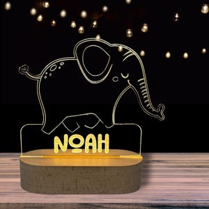 May include: A wooden night light with a clear acrylic elephant design and the name "NOAH" inscribed in gold lettering.